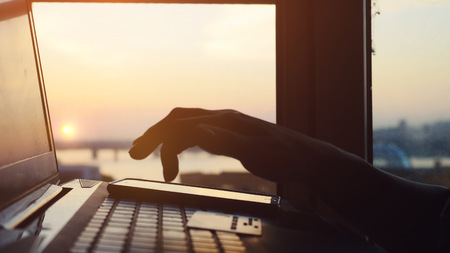 Woman shopping with her laptop on blurred city background during amazing sunset and beautiful sun lense flare effects. Online mobile payment methodの写真素材