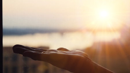 Female hand on blurred city background during beautiful sunset with lense flare effectsの写真素材