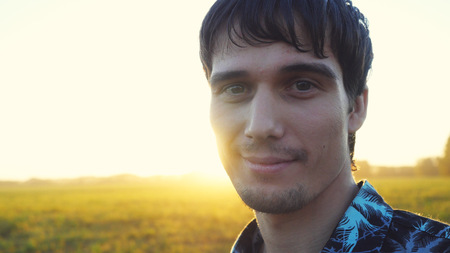 Portrait of smiles man looking at the sun during beautiful sunset with lense flare effects.の写真素材