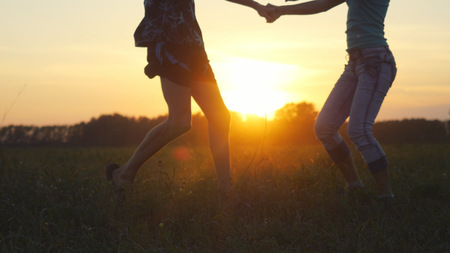 Happy couple having fun outdoors through a field. Countryside. Young man and woman holding hands with sun flare effectの写真素材