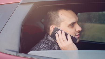 Handsome businessman sitting in car talking on cell phoneの写真素材