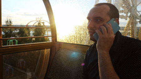 Man talking phone night in a ferris wheel during beautiful sunset and sun flare effects.