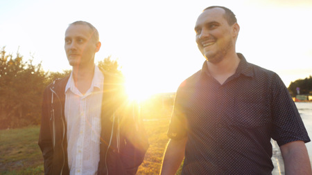 Young men have a serious talk while walking in the city during beautiful sunset with lense flare effectsの写真素材