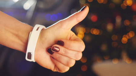 Woman making gestures on a wearable smartwatch computer device and makes thumb up in the end on blurred bokeh christmas tree background.の写真素材