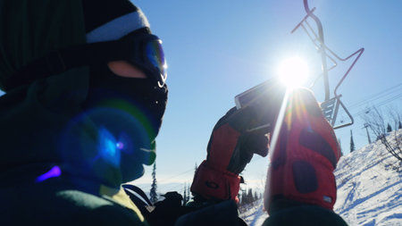 Skier rides in glasses lift chairs on sunny winter day up the beautiful mountain with lense flare effects photographed mountains in the smartphoneの写真素材