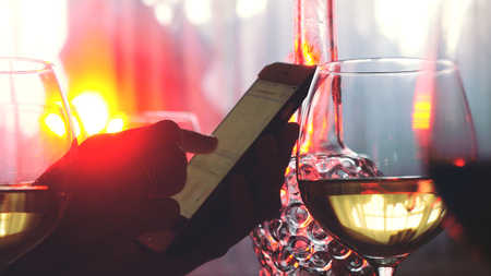 Hands of female uses smartphone and glasses of white wineの写真素材