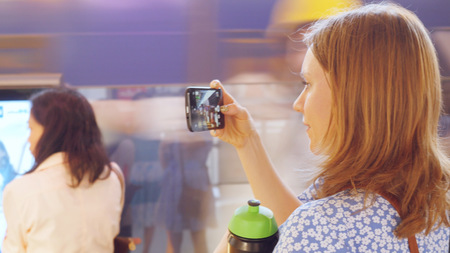 Cheerful woman taking selfie with smartphone in busy train stationの写真素材
