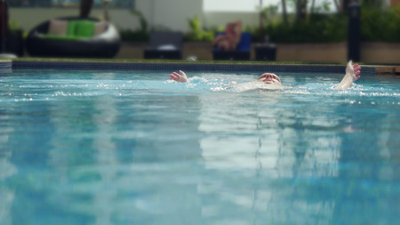 Young man swims on back along city view in swimming poolの写真素材
