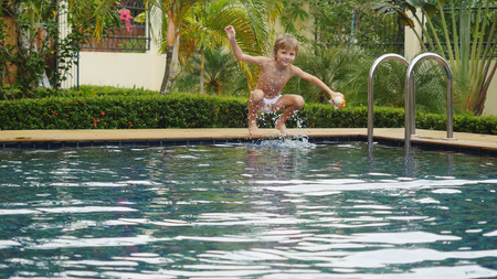Boy splashing water into a swimming poolの写真素材