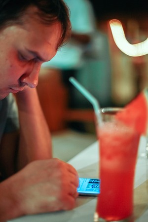 Portrait of young man uses mobile phone with red blur bokeh lights and cocktailの写真素材
