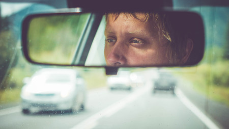 Thoughtful man riding in car through mountains during rainy dayの写真素材