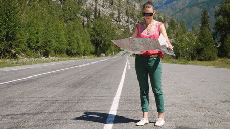 Tourist girl wearing sunglasses holding a map chooses a travel destination on the map.