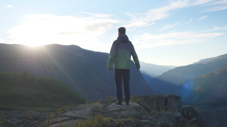 Young man stands high on top of the big mountainand look at beautiful sunset