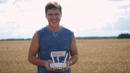 Young happy man controlling drone in field. Drone operator holding a transmitter