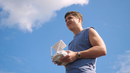 Young man controlling drone in a field on beautiful sky background. Drone operator holding a...