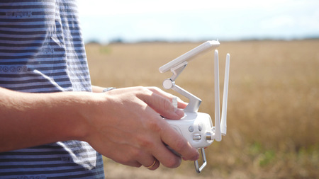 Male hands controlling drone in field. Drone operator holding a transmitterの写真素材