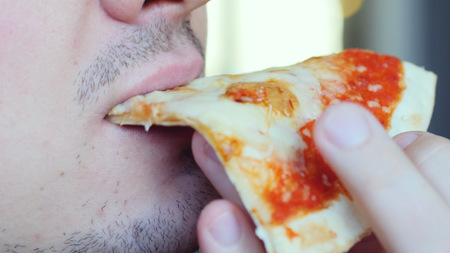 Close up of a man eating a slice of pizza on blurred bokeh backgroundの写真素材