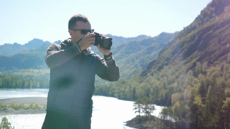 Young man in sunglasses taking picture with professional camera in the mountain on nature.