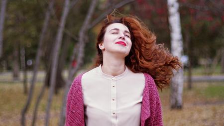 Portrait of autumn smiles young woman with red hair in fall forest in a beautiful colorful forest foliage.の写真素材