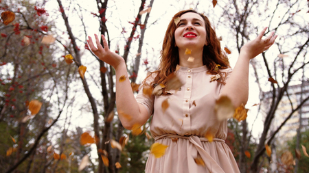 Happy young woman with red curly hair throwing leaves in an autumn fall park.の写真素材