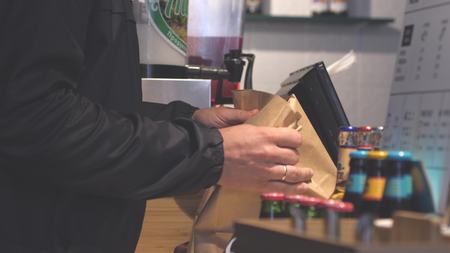 Close up of male hands putting burgers into bag. Man buys packaged food in cafe.の写真素材