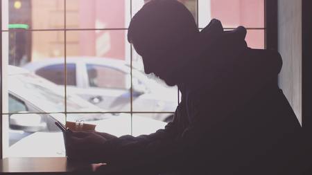 Man using mobile phone and drinking coffee in cafe by the window.の写真素材