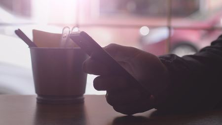 Close up of men hands use mobile phone and drinks coffee by the window in cafe.の写真素材