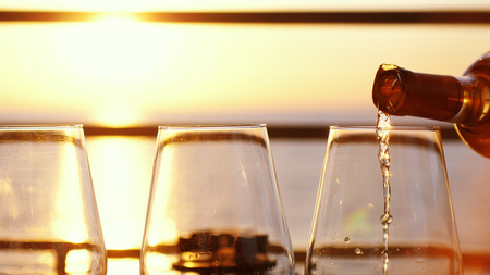 Pouring white wine in a clear glasses at amazing sunset by the sea in beach cafe.の写真素材