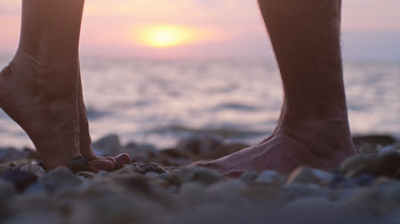 Legs of couple in love during the date near the sea on the beach during beautiful sunset.