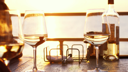 A romantic dinner in summer on a beach at sunset with two glasses of white wine and a bottle of the wineの写真素材