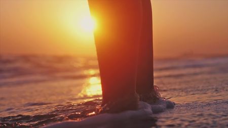 Close up of young woman feet standing near the sea during beautiful sunsetの写真素材