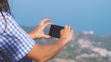 Female tourist takes photo on the phone a wonderfully beautiful view of the blue sea and mountains. Close upの写真素材