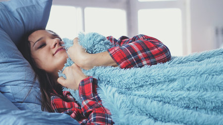 Sleepy young woman lying in bed waking up and stretches
