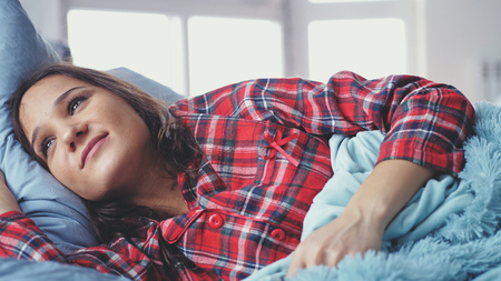 Young woman sleeping in bed and waking up in the morning and smilingの写真素材