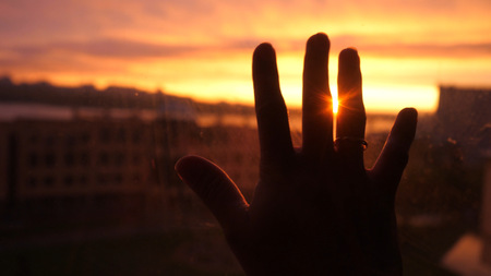 Women hand touches the sun by the window on amazing sunset city backgroundの写真素材