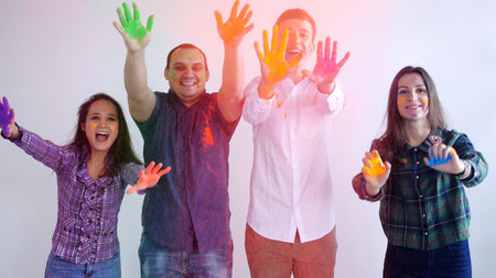 Funny friends throw the paint from hands directly to the camera while standing in studio by the...