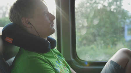 Young handsome man with pillow listening to music while rides on busの写真素材