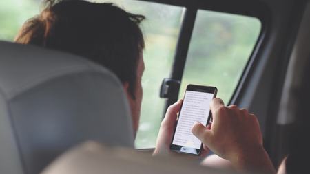 Young man reads a book on the phone while riding a busの写真素材