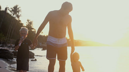 Dad holding childrens hands at beautiful sunset and walking on tropical beach. Travel holiday...