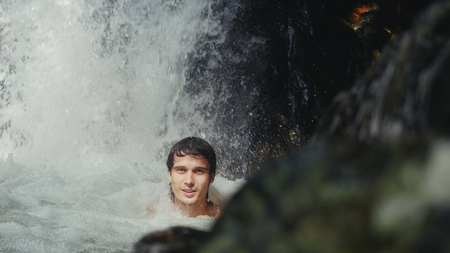 Happy handsome man relaxing under stream water in waterfall in tropical jungle.の写真素材