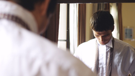 Young man in white shirt stands by the mirror tying a tieの写真素材