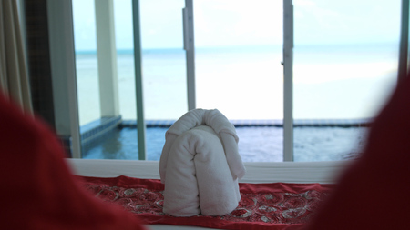 Hotel bed in luxury hotel room with white bedding. Welcome resort decor on hot tub and the sea on foreground. Towel is made in the form of an elephantの写真素材