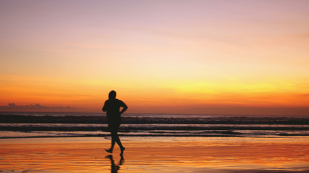 Silhouette of fat man runs along the beach during amazing sunset.の写真素材