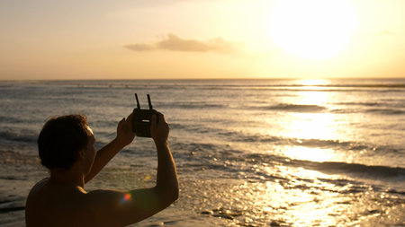 Man operating a drone with remote control. Quadro copter drone flying over sunset ocean