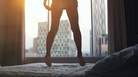 Happy young sexy woman jumping on bed in luxury apartment at sunset time. lose upの写真素材