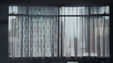 Cityscape view through modern window and transperent curtains in roomの写真素材