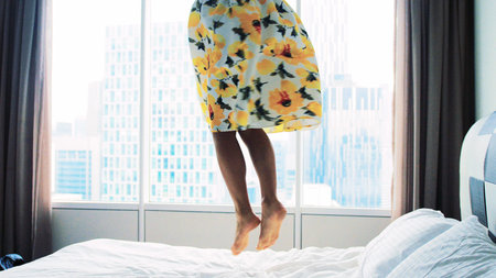Happy woman wearing beautiful dress dances jumps on bed at home
