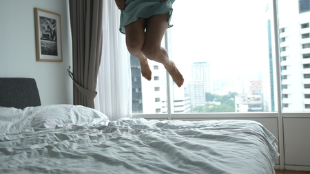 Happy young woman jumping on bed at home having fun in the bed in a luxury apartment with city viewの写真素材