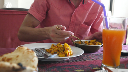 Young man eats chicken curry potato in indian cafe.の写真素材