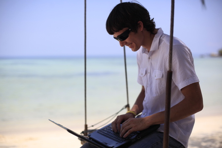 Traveler man relaxing on swing at beautiful landscape white sand beach using laptop, Businessman on summer vacation trip,の写真素材